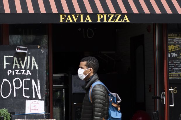 A man walks by a pizza restaurant while wearing a face mask in...