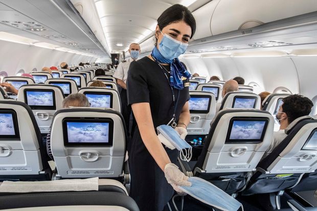 A flight attendant distributes masks on a flight at Cairo airport. Mask-wearing and air filtration...