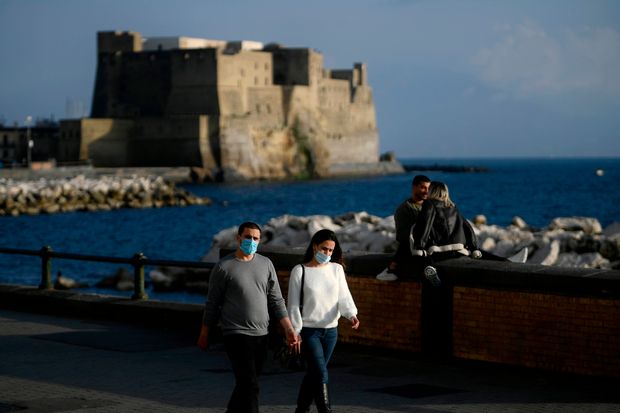 People wearing face masks stroll and relax along the seafront near the Castel dell'Ovo fortress...